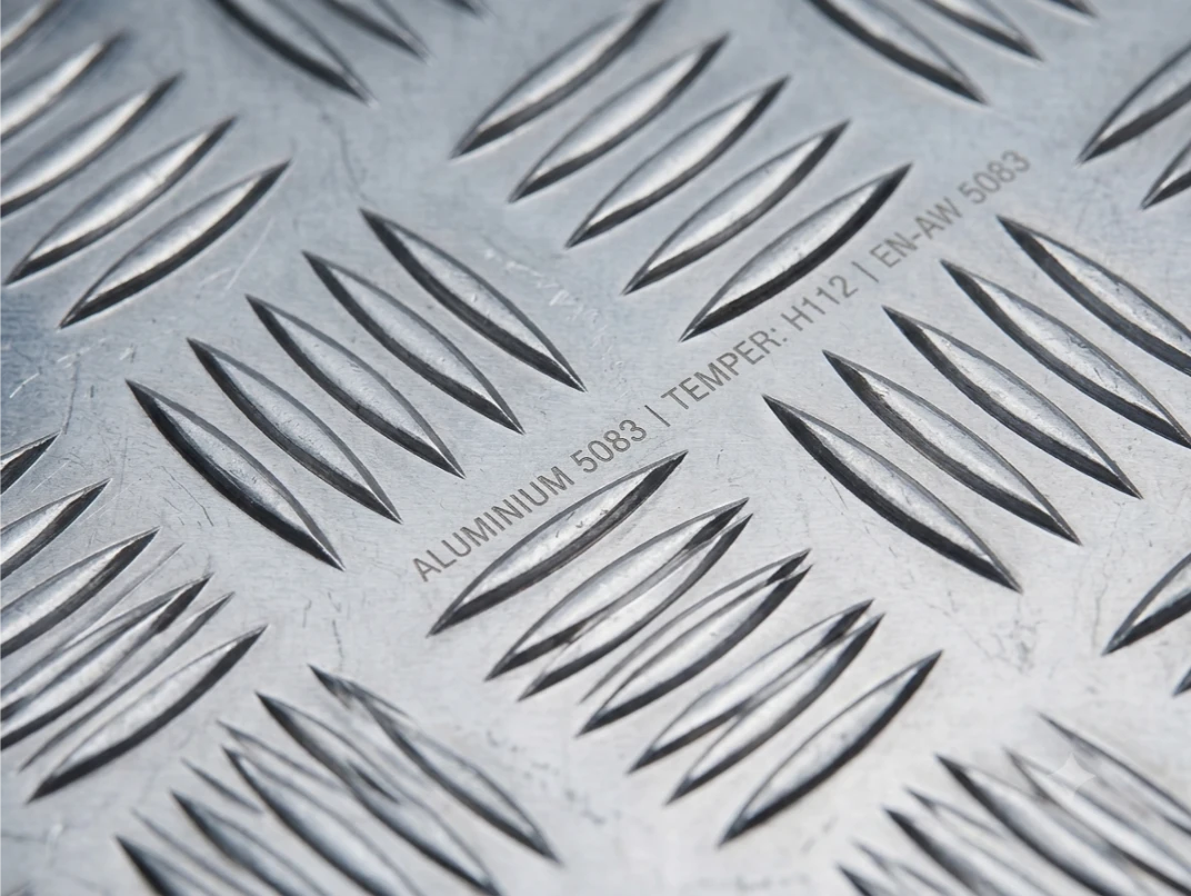  Close-up angled view of 5083 aluminium chequered plate showing raised 5-bar anti-slip tread pattern and grade stamp